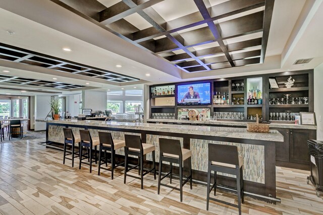 bar with light stone countertops, light hardwood / wood-style floors, and coffered ceiling