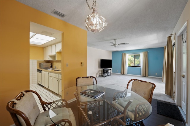 dining space with sink, light colored carpet, a textured ceiling, ceiling fan with notable chandelier, and a skylight