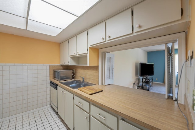 kitchen featuring white cabinetry, light tile patterned flooring, dishwashing machine, tile walls, and sink