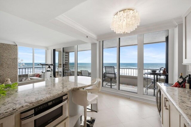 kitchen with a water view, a chandelier, stainless steel oven, and light stone countertops