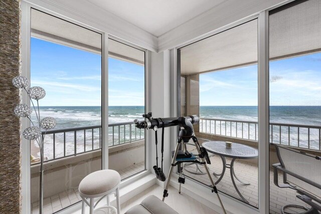 sunroom featuring a water view, a view of the beach, and plenty of natural light