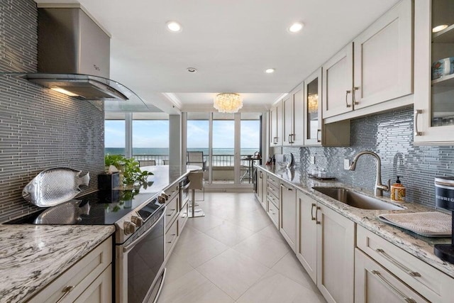 kitchen featuring light tile patterned flooring, tasteful backsplash, wall chimney range hood, sink, and stainless steel range with electric stovetop