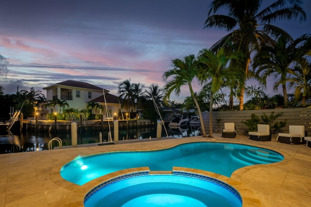 pool at dusk featuring a patio, an in ground hot tub, and a water view