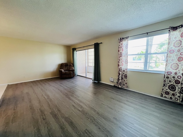 empty room featuring a textured ceiling, dark wood-type flooring, and a healthy amount of sunlight