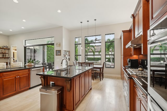 kitchen featuring sink, appliances with stainless steel finishes, hanging light fixtures, and a center island with sink