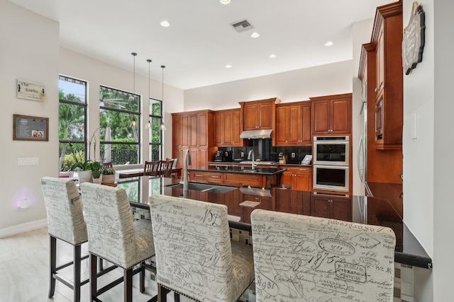 kitchen featuring decorative backsplash, stainless steel double oven, pendant lighting, and a breakfast bar