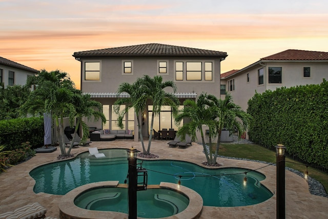 pool at dusk featuring an in ground hot tub and a patio area