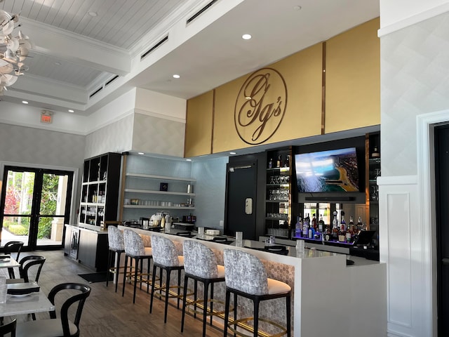 bar featuring beam ceiling, french doors, a high ceiling, hardwood / wood-style floors, and ornamental molding