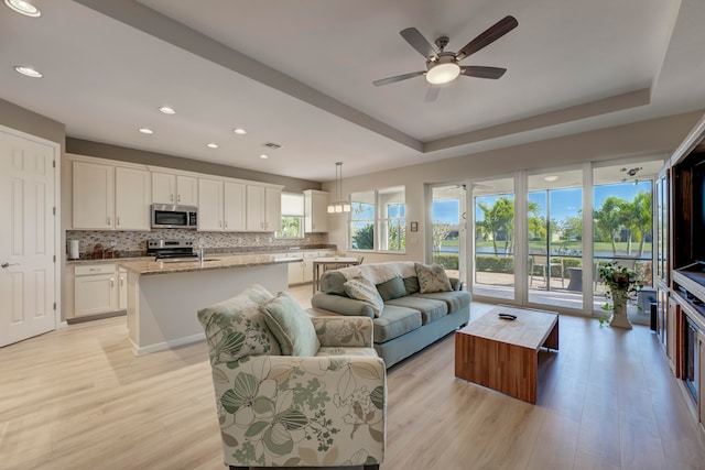 living room featuring a raised ceiling, sink, light wood-type flooring, and ceiling fan