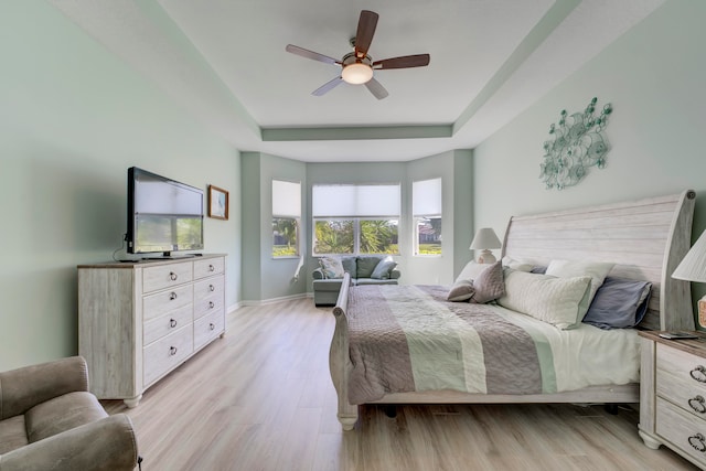 bedroom with a raised ceiling, ceiling fan, and light wood-type flooring