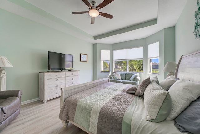 bedroom featuring multiple windows, light wood-type flooring, ceiling fan, and a raised ceiling