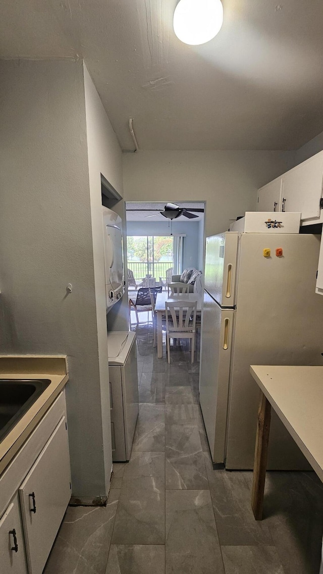 kitchen with light countertops, stacked washer and clothes dryer, marble finish floor, white cabinetry, and freestanding refrigerator