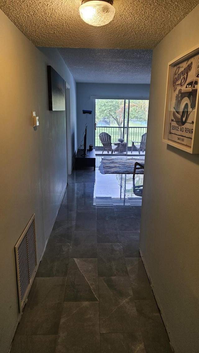 corridor featuring baseboards, visible vents, and a textured ceiling