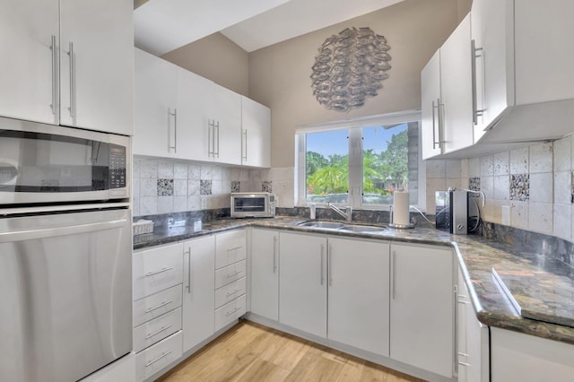 kitchen with backsplash, stainless steel microwave, sink, light hardwood / wood-style flooring, and white cabinetry