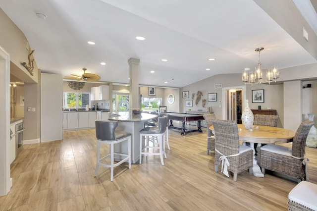 dining space with light wood-type flooring, ceiling fan with notable chandelier, lofted ceiling, and ornate columns