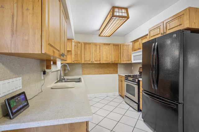 kitchen featuring light brown cabinetry, black refrigerator, stainless steel range with gas cooktop, sink, and light tile patterned floors