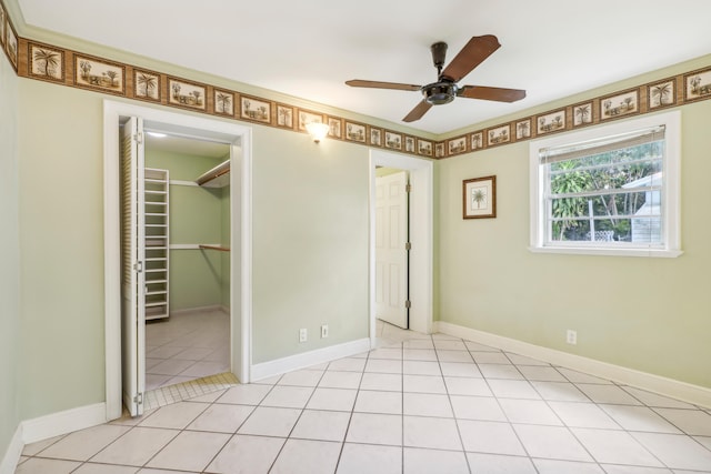 unfurnished bedroom with a closet, a walk in closet, light tile patterned floors, and ceiling fan