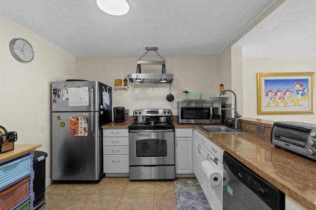 kitchen featuring light tile patterned flooring, a sink, white cabinets, appliances with stainless steel finishes, and wall chimney exhaust hood