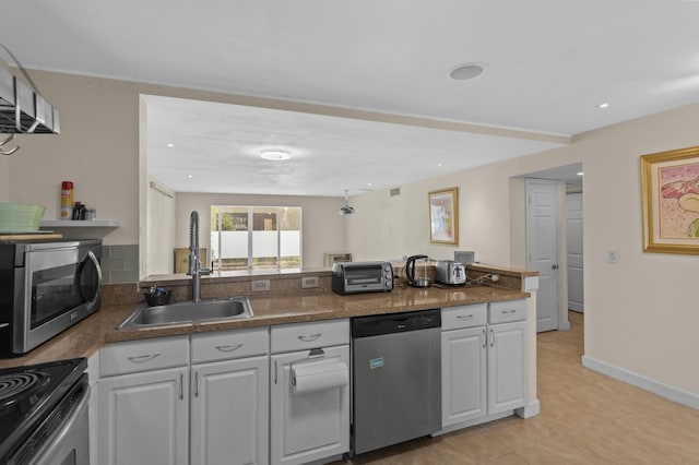 kitchen featuring stainless steel appliances, a peninsula, a sink, baseboards, and white cabinets