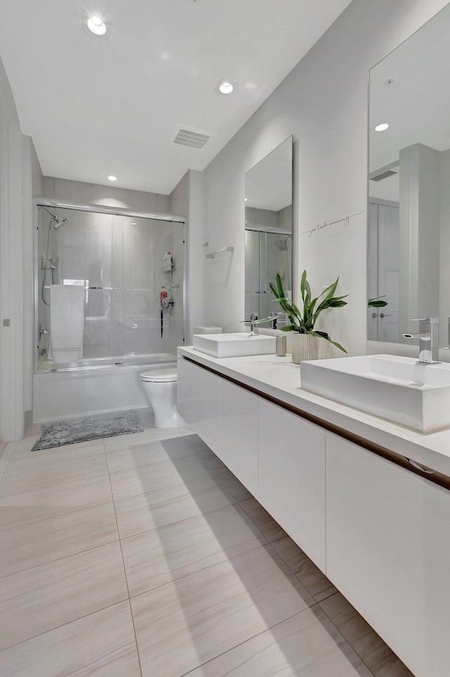 full bathroom featuring combined bath / shower with glass door, tile patterned floors, dual vanity, and toilet