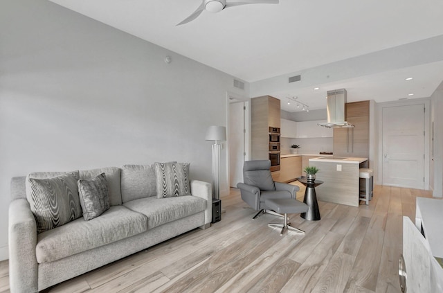 kitchen with a kitchen bar, a kitchen island, light hardwood / wood-style floors, double oven, and island range hood