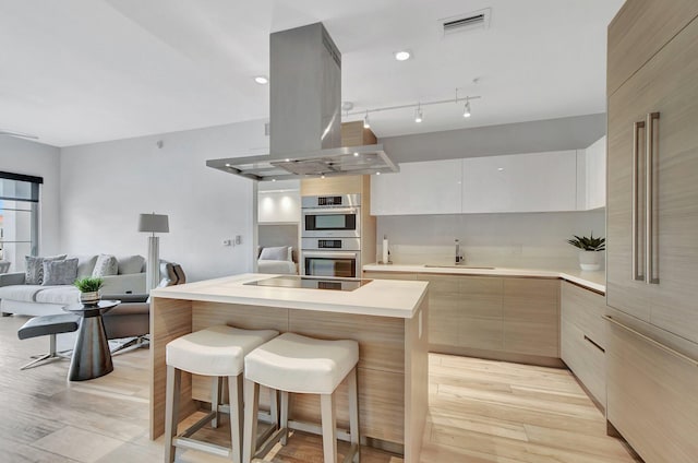 kitchen with island range hood, sink, rail lighting, light wood-type flooring, and double oven