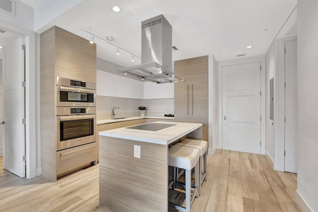 kitchen featuring light hardwood / wood-style flooring, a breakfast bar, a kitchen island, island exhaust hood, and double oven