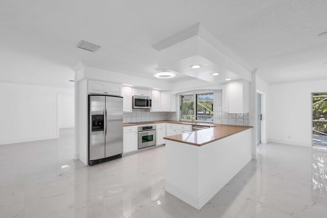 kitchen with appliances with stainless steel finishes, white cabinetry, decorative backsplash, sink, and kitchen peninsula