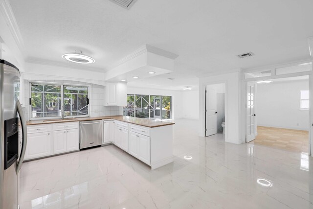 kitchen with kitchen peninsula, white cabinets, ornamental molding, decorative backsplash, and stainless steel appliances