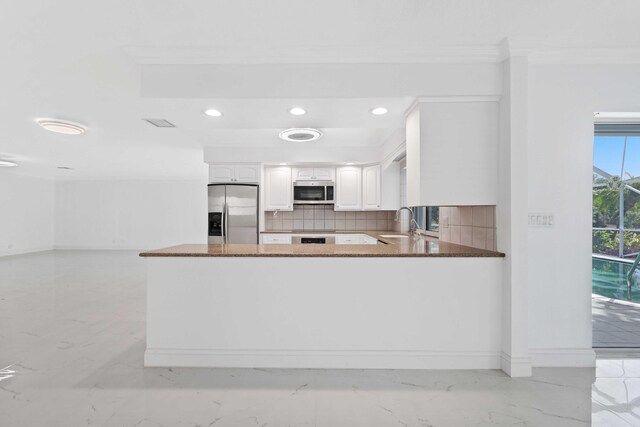 kitchen featuring kitchen peninsula, dark stone countertops, appliances with stainless steel finishes, white cabinets, and ornamental molding