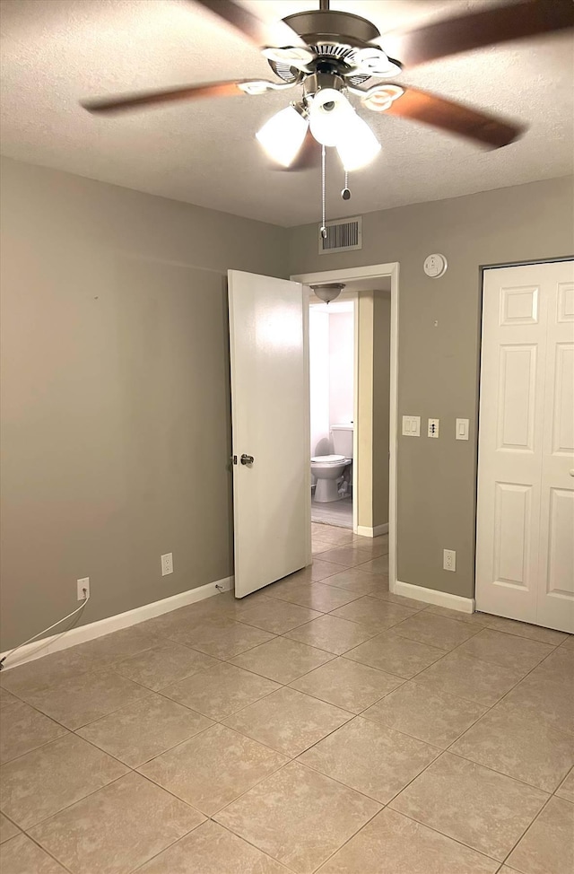 tiled empty room with ceiling fan and a textured ceiling