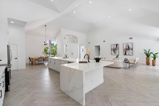 kitchen featuring light parquet floors, high vaulted ceiling, a center island with sink, and light stone countertops