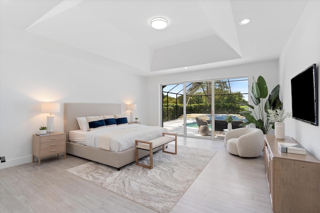 bedroom featuring light wood-type flooring, a tray ceiling, and access to outside