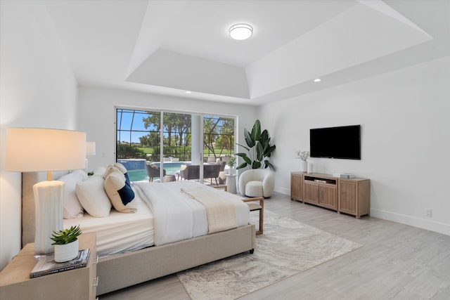 bedroom featuring light wood-type flooring, a raised ceiling, and access to exterior