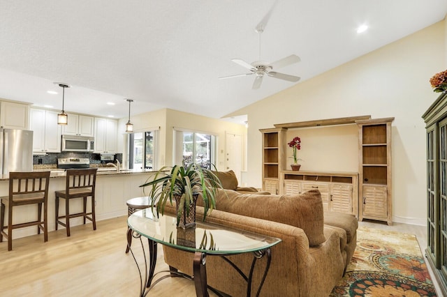 living room featuring vaulted ceiling, sink, ceiling fan, and light hardwood / wood-style flooring