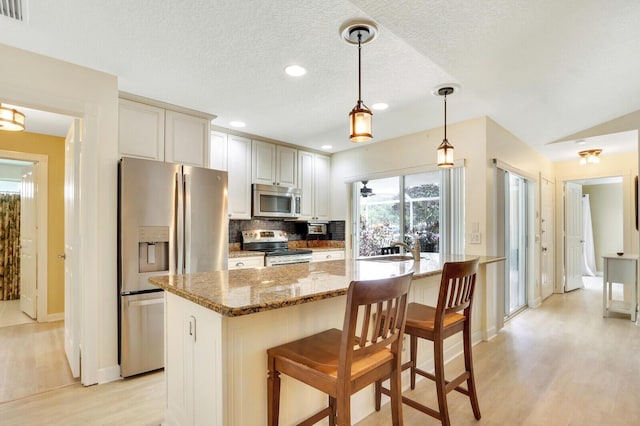 kitchen with stainless steel appliances, an island with sink, hanging light fixtures, and stone countertops