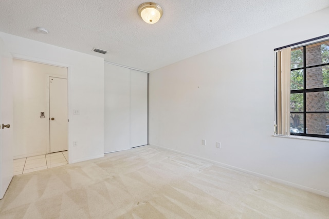 unfurnished bedroom featuring light colored carpet, a closet, and a textured ceiling