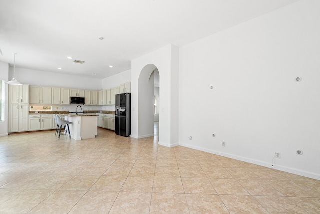 kitchen with black fridge with ice dispenser, light tile patterned flooring, a kitchen bar, and an island with sink