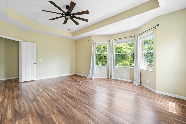 empty room with ceiling fan, hardwood / wood-style flooring, and a tray ceiling