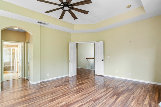 empty room featuring hardwood / wood-style flooring, a raised ceiling, and ceiling fan