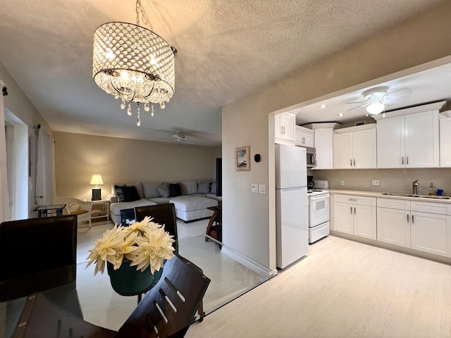 kitchen featuring white appliances, white cabinets, a textured ceiling, sink, and hanging light fixtures