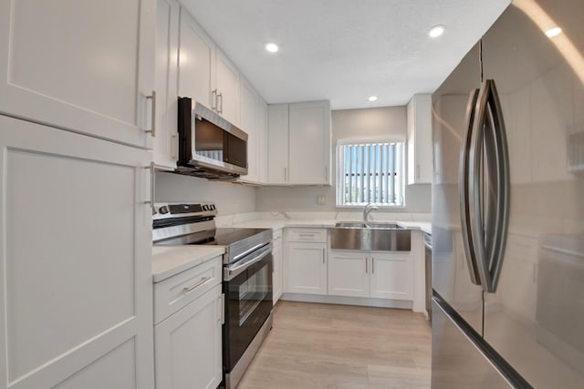 kitchen featuring sink, light stone counters, light hardwood / wood-style flooring, white cabinets, and appliances with stainless steel finishes