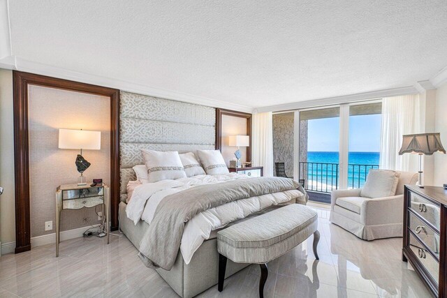 bedroom featuring a water view, a textured ceiling, expansive windows, and access to exterior