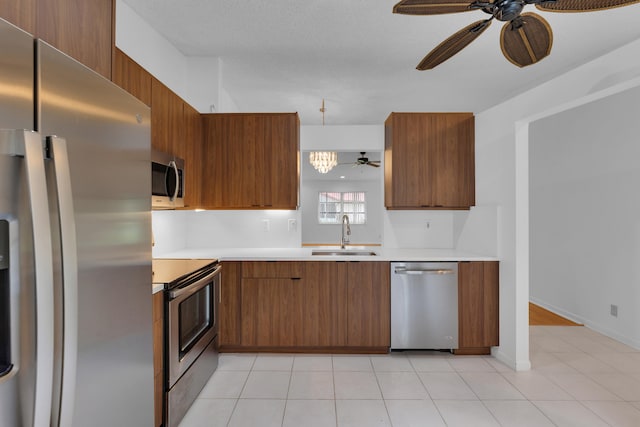 kitchen with light tile patterned floors, stainless steel appliances, ceiling fan with notable chandelier, and sink