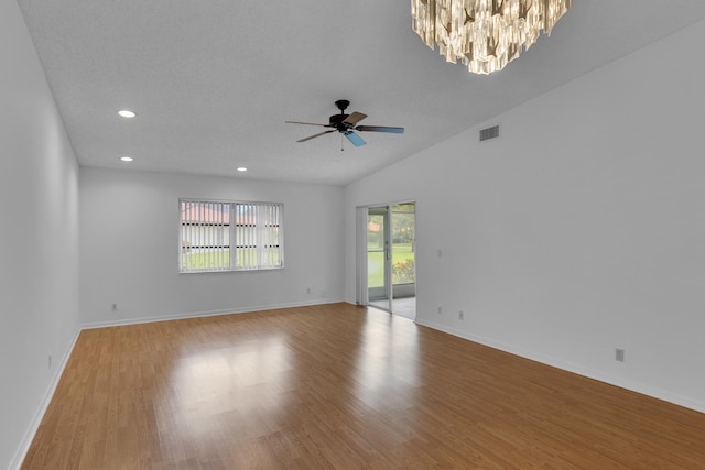 empty room featuring ceiling fan with notable chandelier, light hardwood / wood-style flooring, and vaulted ceiling