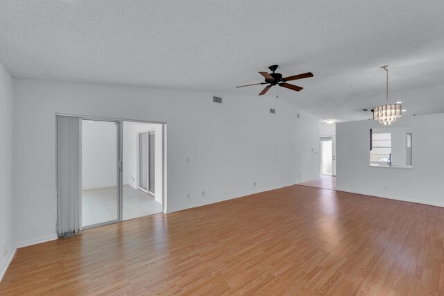 unfurnished living room featuring ceiling fan with notable chandelier, a textured ceiling, light hardwood / wood-style flooring, and vaulted ceiling