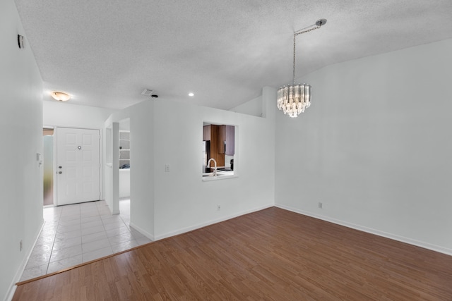 unfurnished room featuring a notable chandelier, vaulted ceiling, light wood-type flooring, and a textured ceiling