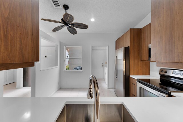 kitchen with light tile patterned flooring, a textured ceiling, ceiling fan, and stainless steel appliances