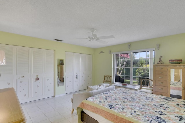 bedroom featuring ceiling fan, two closets, a textured ceiling, and light tile patterned flooring