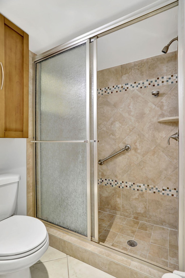 bathroom featuring tile patterned flooring, a shower with shower door, and toilet